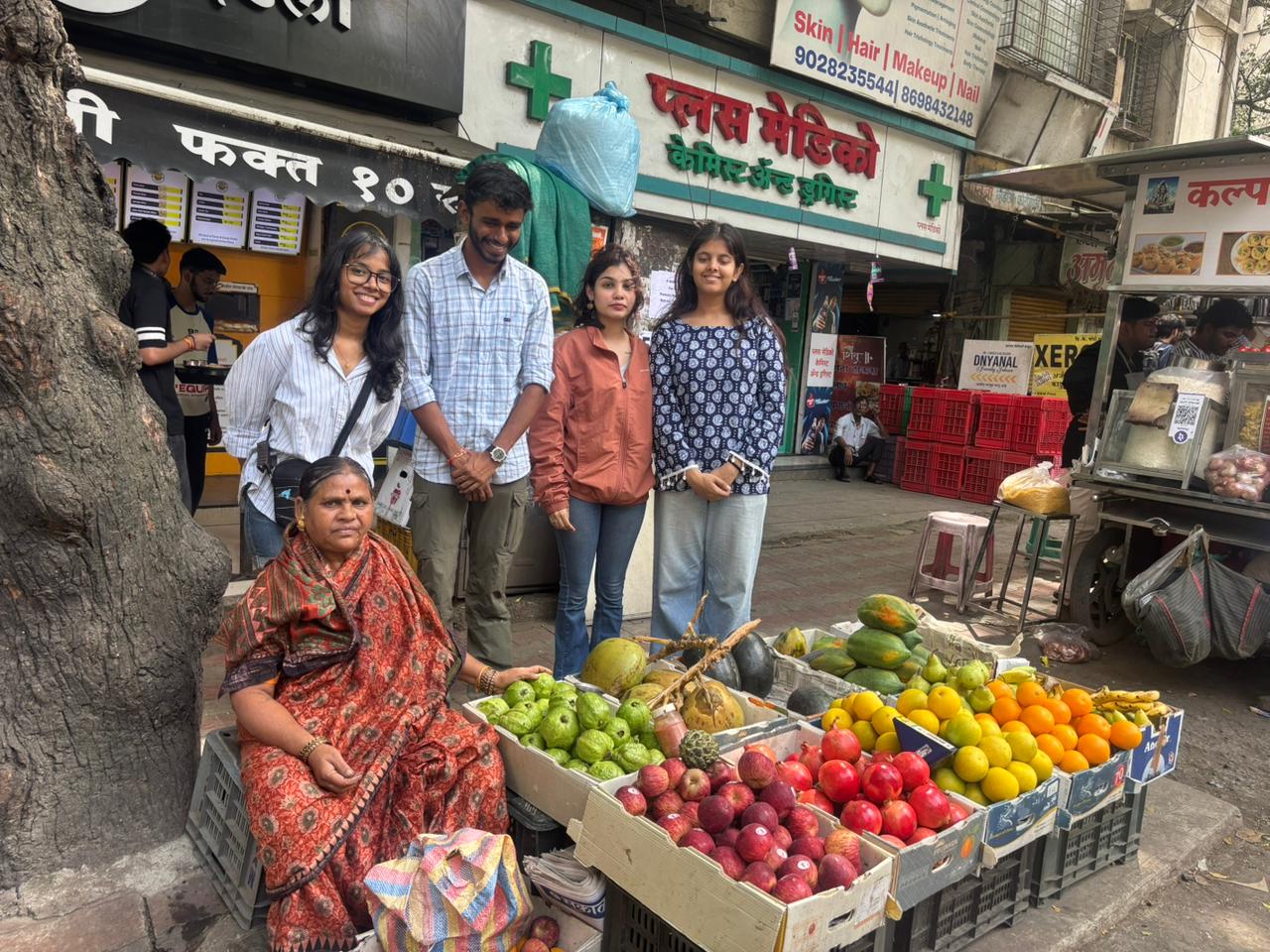 MEER India field team photographed with a fruit vendor beside her produce crates on FC Road, Pune