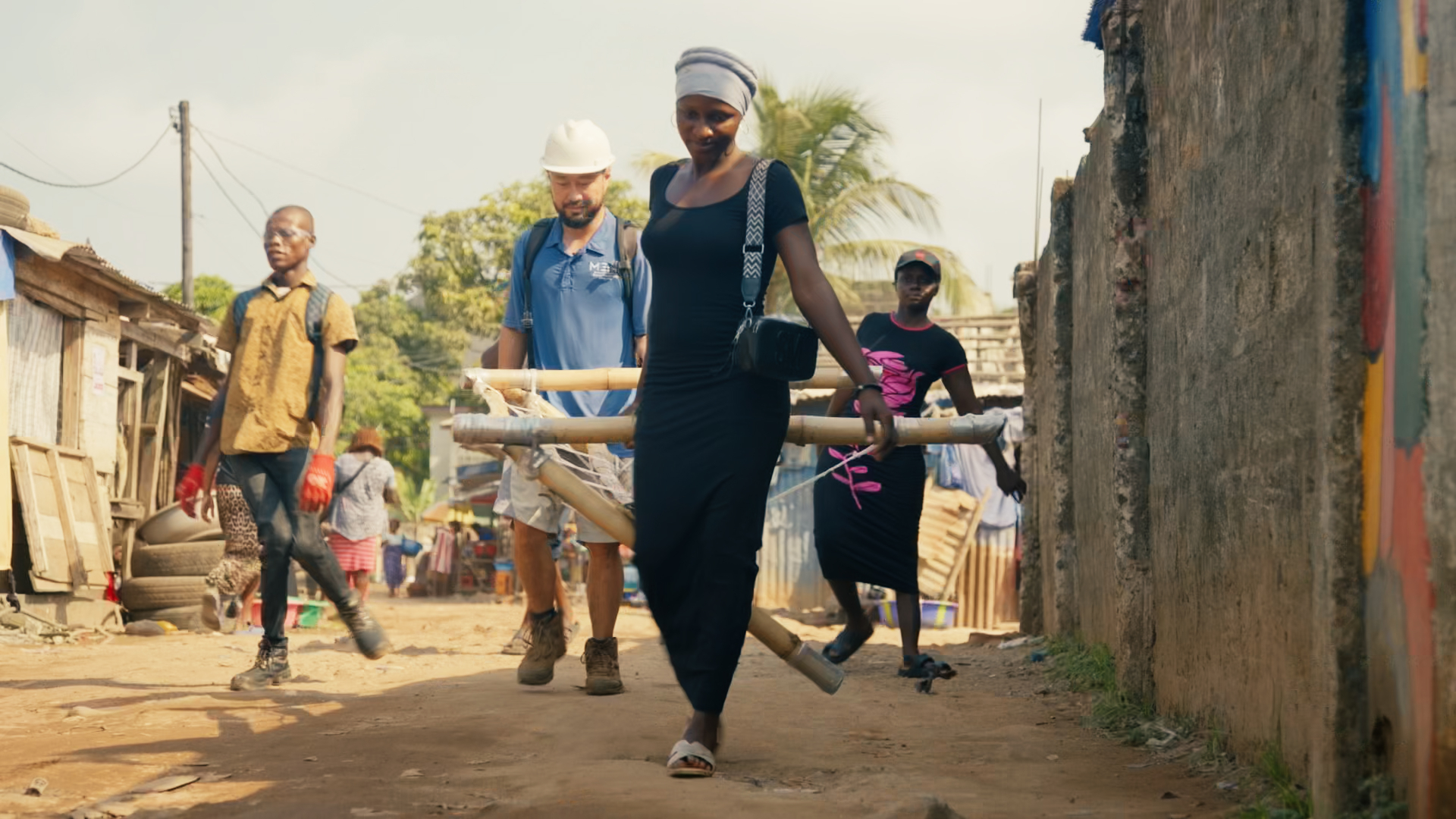 MEER team members walking through a Sierra Leone neighbourhood carrying bamboo beams for a cooling installation