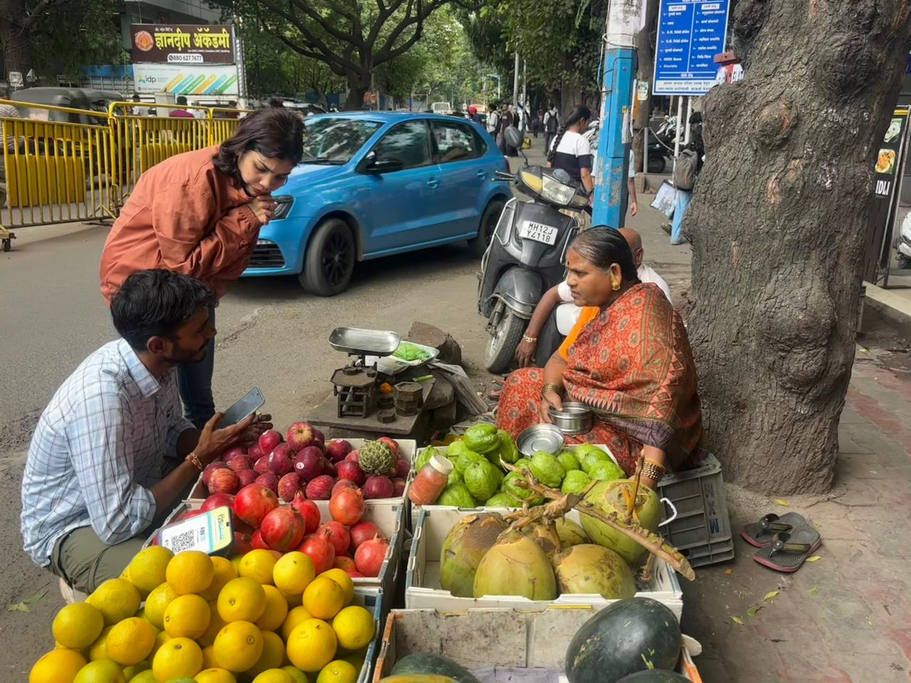 A MEER researcher crouching beside a seated fruit vendor to record survey responses at a roadside stall in Pune