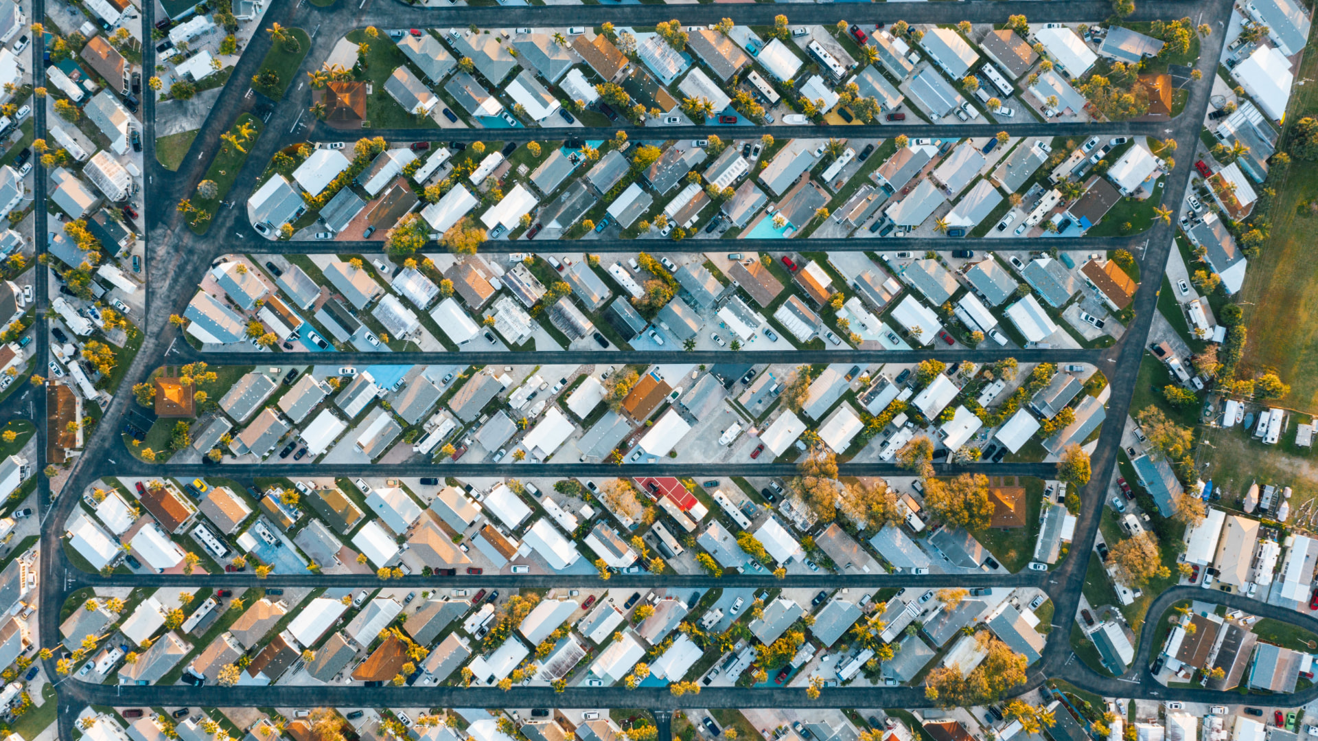 Aerial view of a densely packed manufactured housing park with rows of mobile homes, palm trees and parked cars